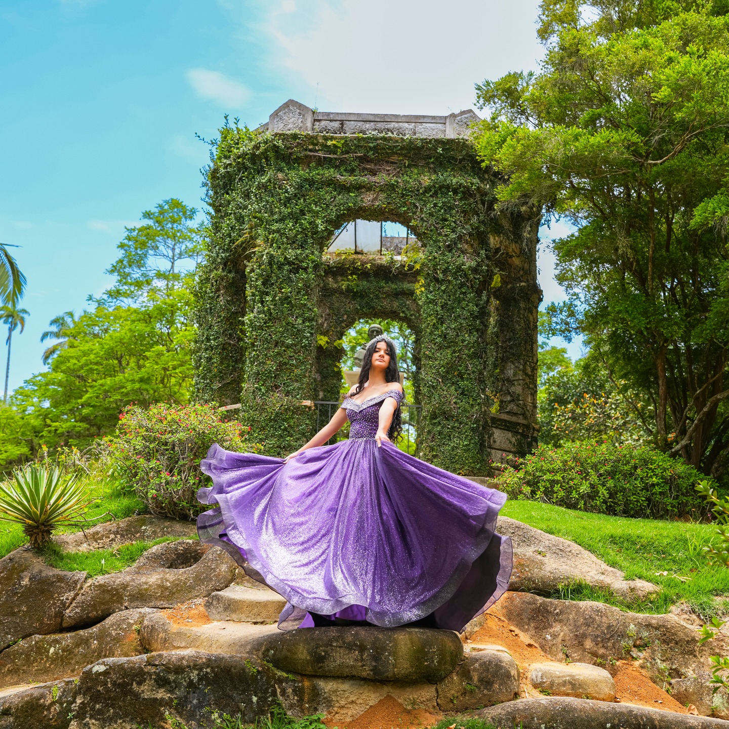 Debutante em vestido lilás rodopiando em frente a um jardim com ruínas cobertas de hera