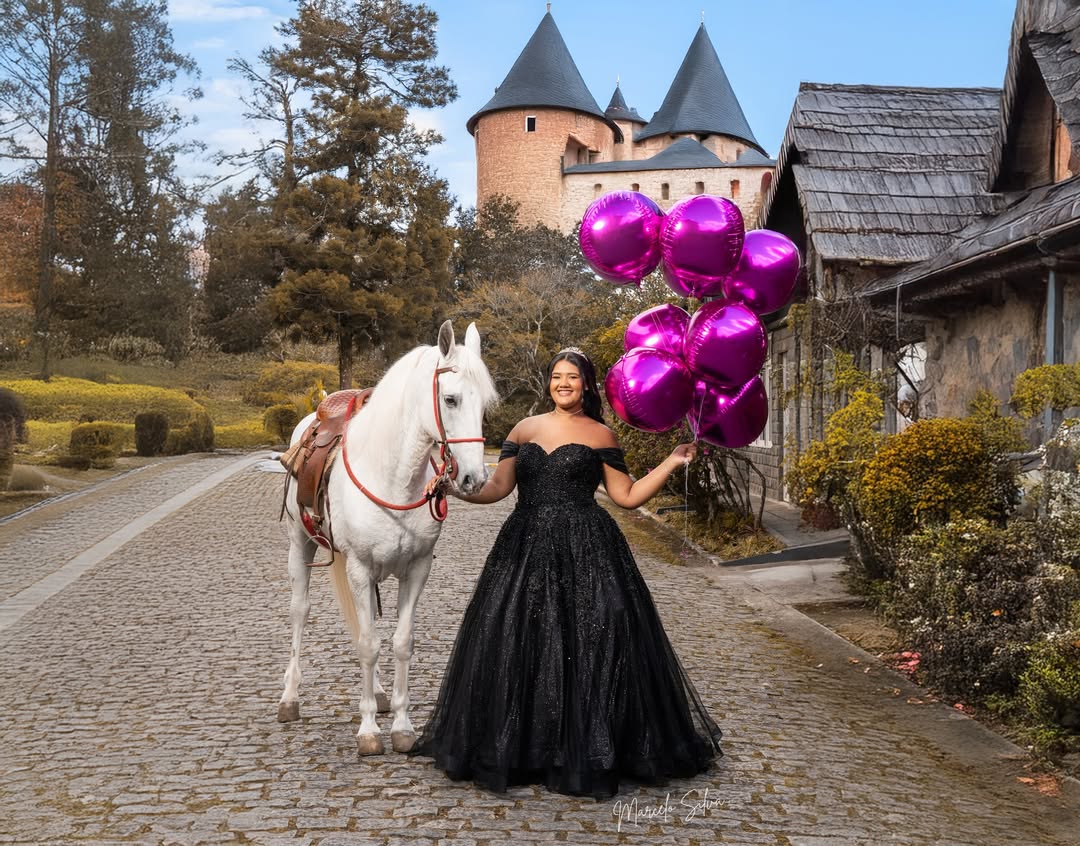 Debutante em vestido preto ao lado de um cavalo branco, com balões e um castelo ao fundo
