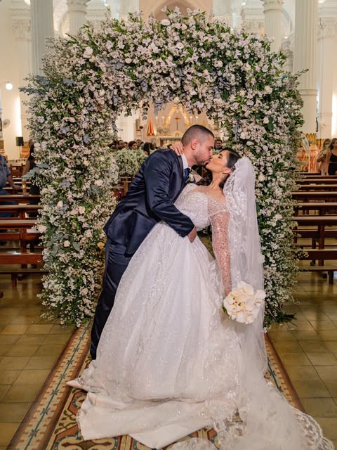 Noivos se beijando em frente a arco de flores na cerimônia de casamento