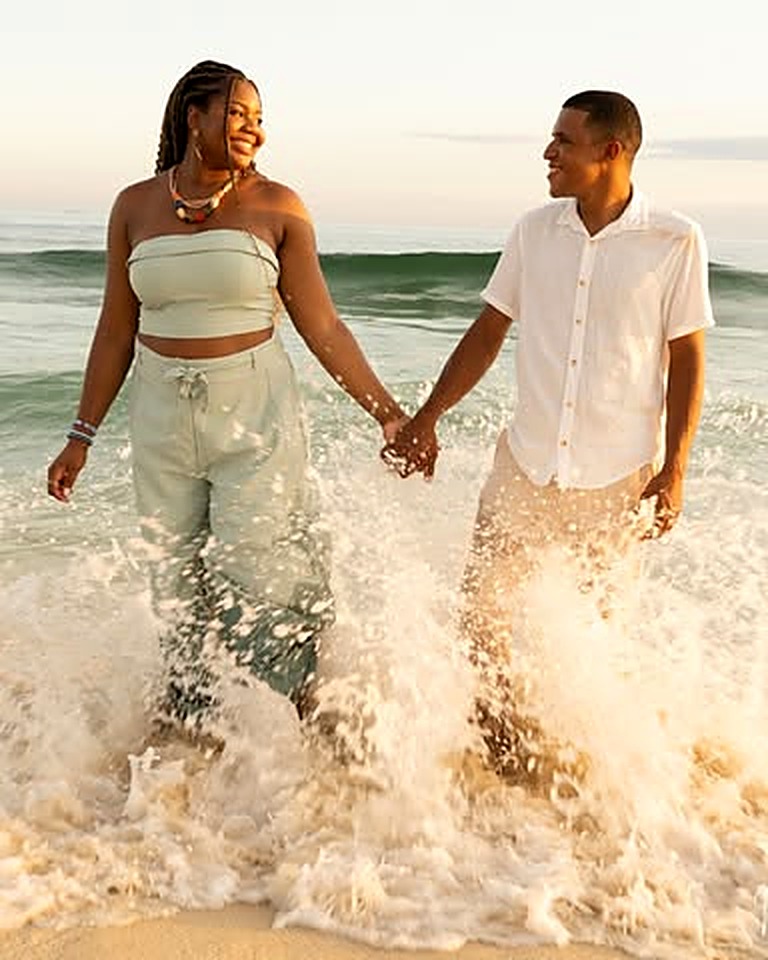 Noivos de mãos dadas caminhando na praia com as ondas do mar